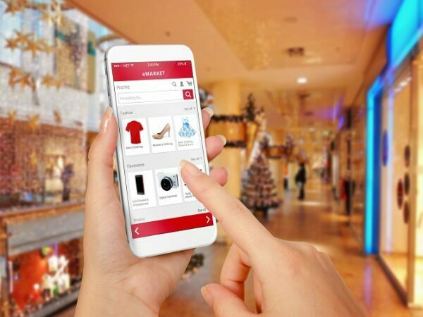 Smart phone online shopping in woman hand during Christmas. Shopping center in background. Buy clothes shoes accessories with e commerce web site