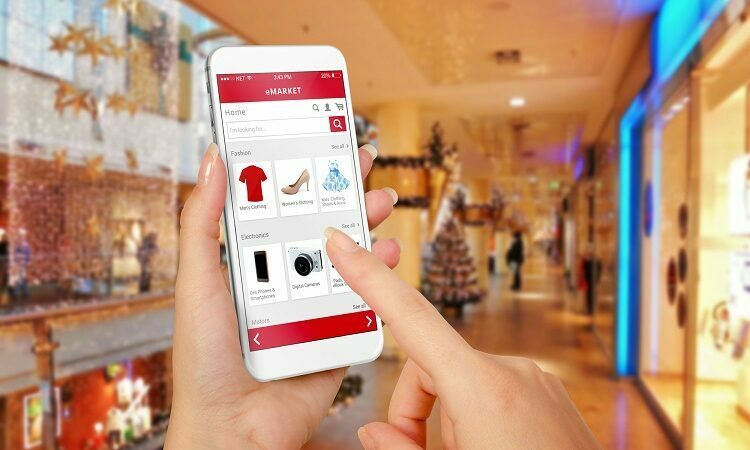 Smart phone online shopping in woman hand during Christmas. Shopping center in background. Buy clothes shoes accessories with e commerce web site